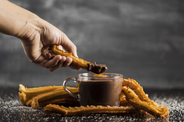 mano-sumergiendo-un-churros-fritos-en-vista-frontal-de-chocolate