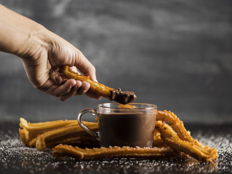 mano-sumergiendo-un-churros-fritos-en-vista-frontal-de-chocolate